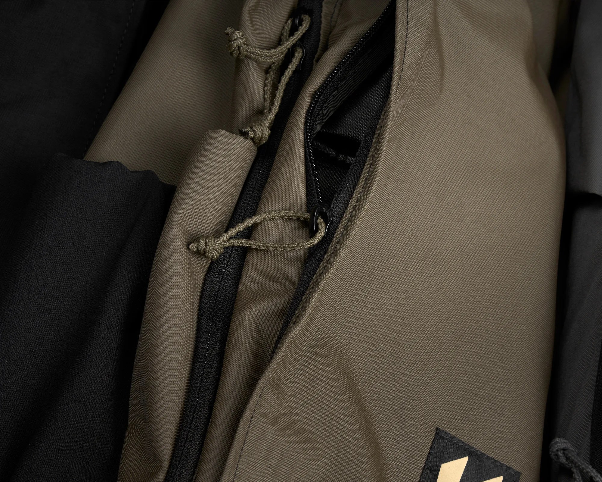 Close-up of a khaki fabric jacket with black zipper and braided pull cords.