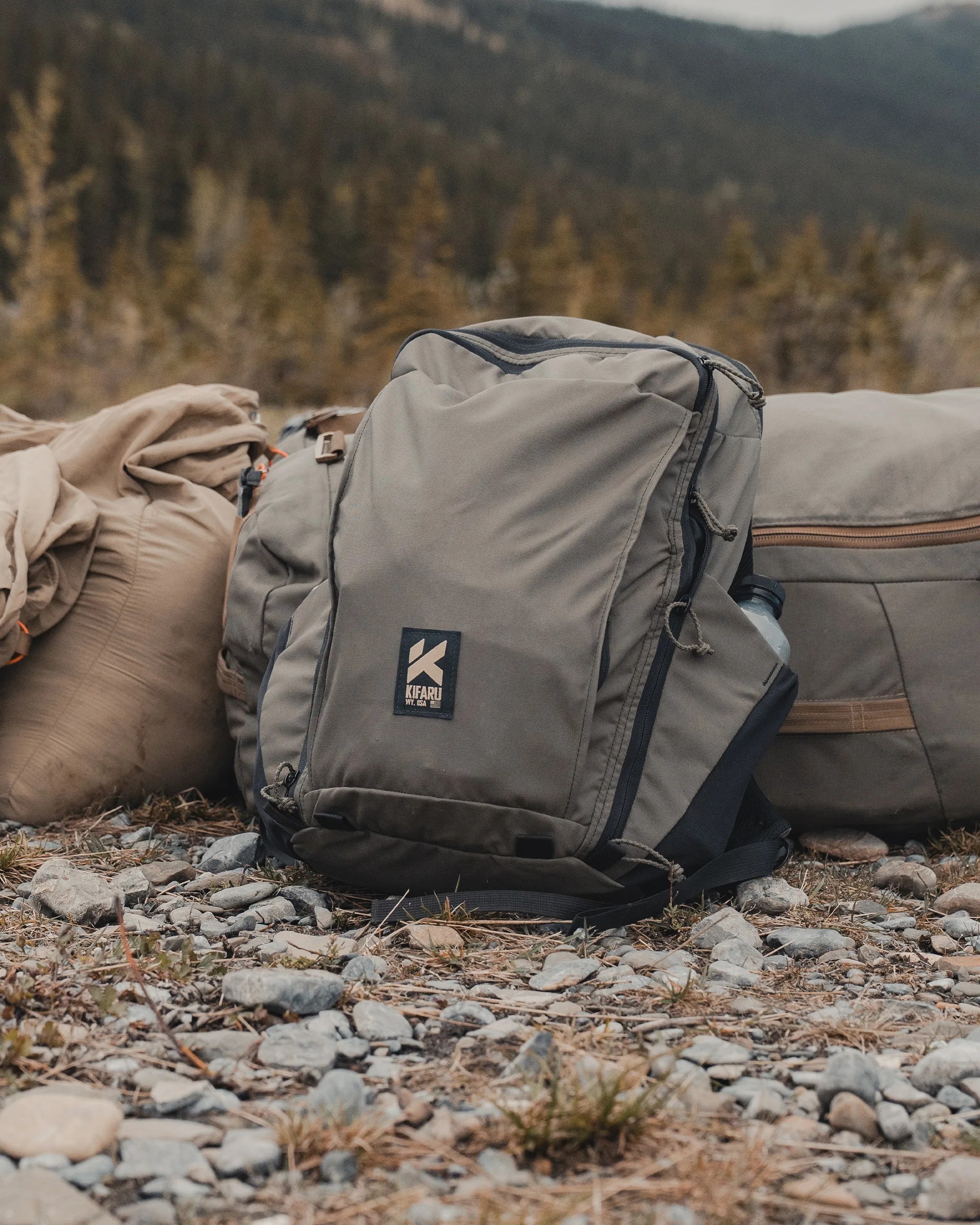 Gray Kifaru backpack with multiple compartments resting on rocky ground outdoors.