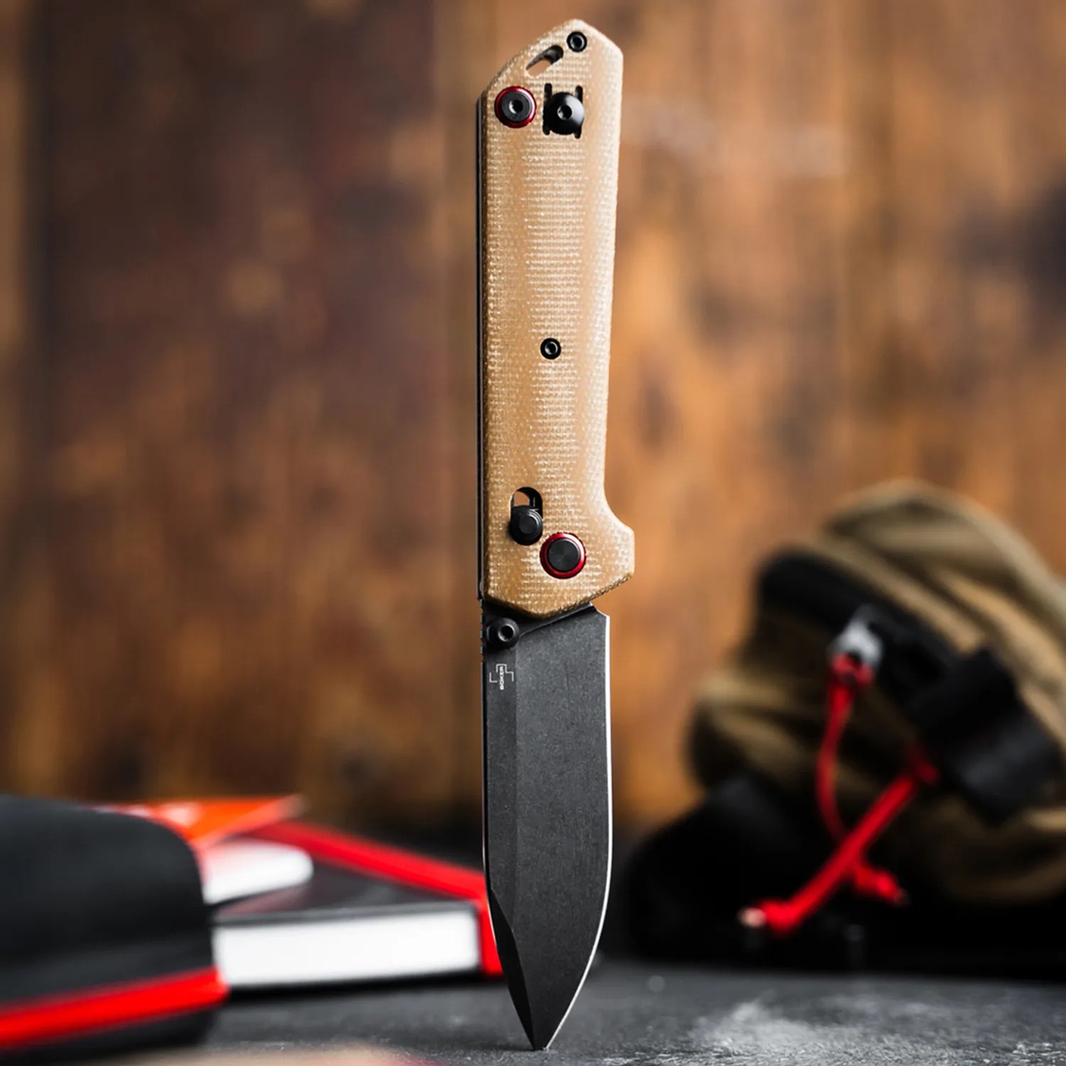 Folding knife with tan textured handle and black blade standing upright on a dark surface.