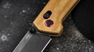 Close-up of a folding knife with a tan textured handle and a partially visible black blade on a dark surface.