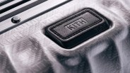 Close-up of a silver textured suitcase with a black leather patch embossed with "KITH" and "TUMI" logos.