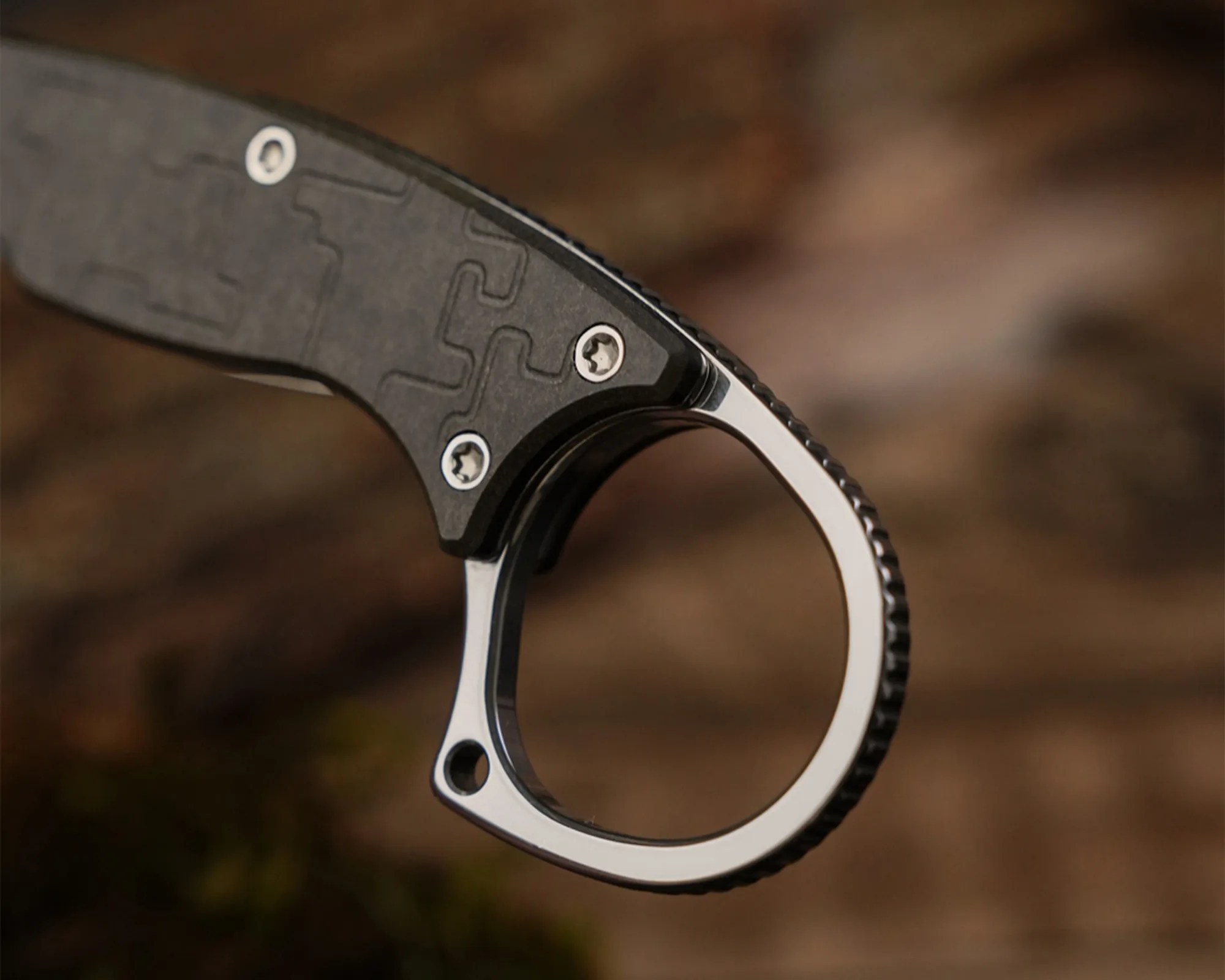 Close-up of a black knife handle with a textured grip and a silver finger ring at the end.