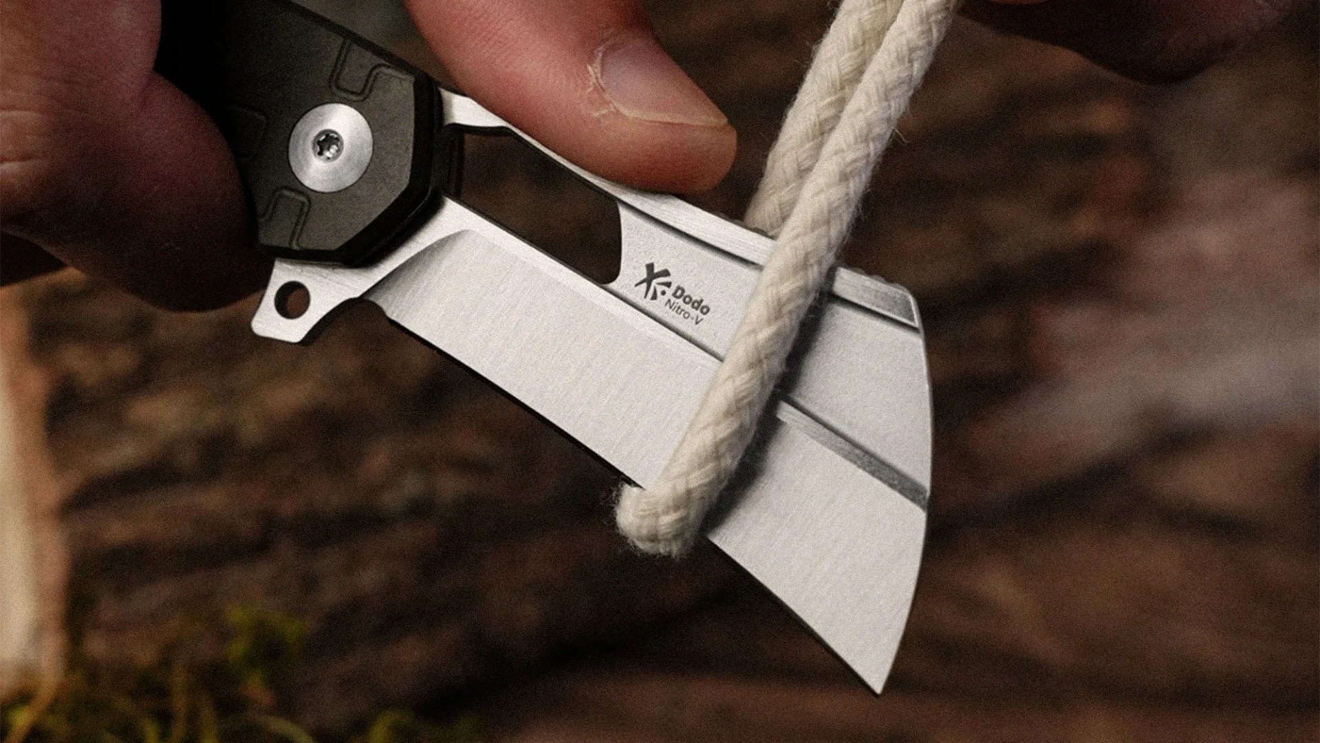 Close-up of a hand holding a folding knife with a silver blade cutting a white rope.