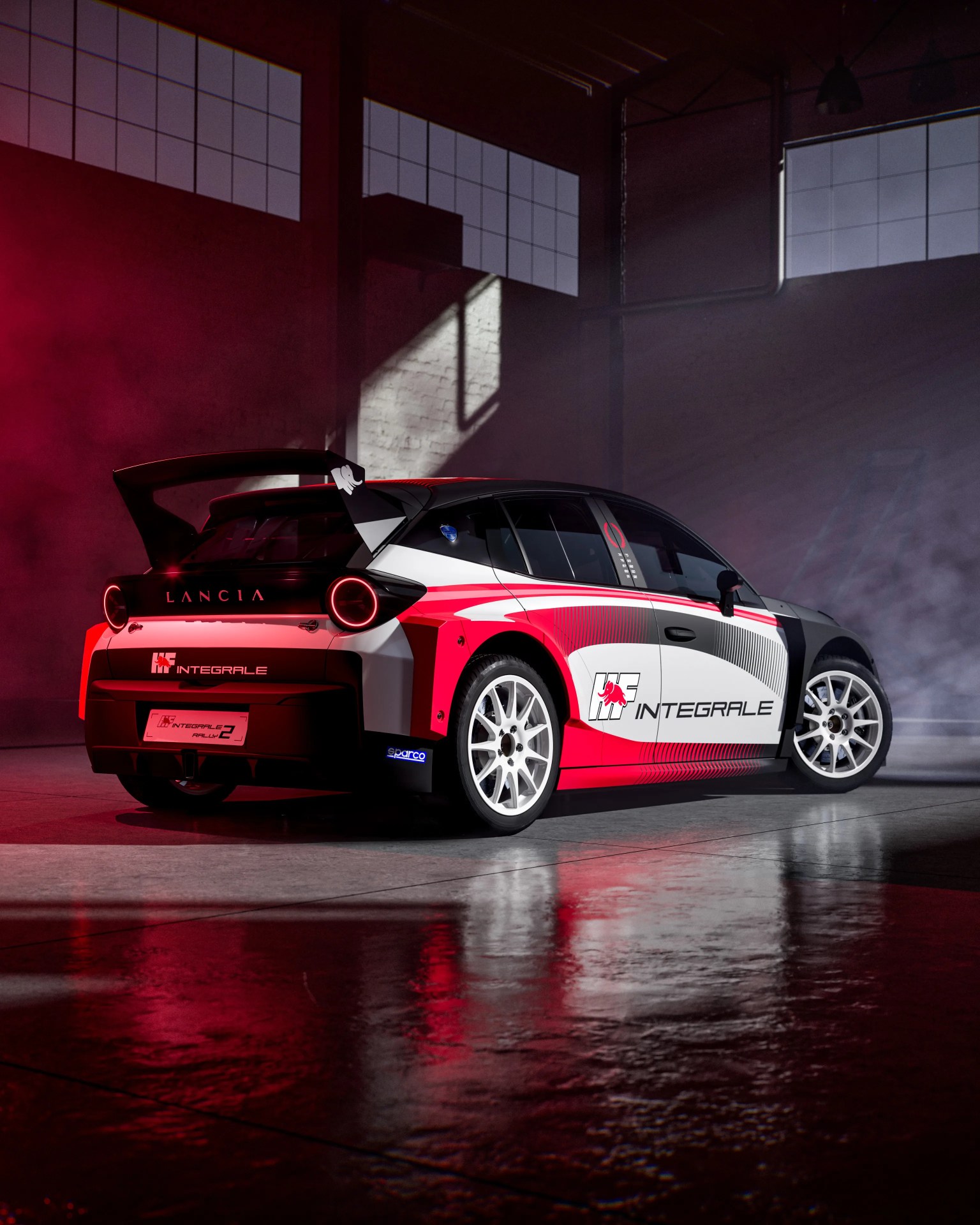 White, red, and black Lancia Integrale rally car with large rear wing in a dimly lit garage with red and white lighting.