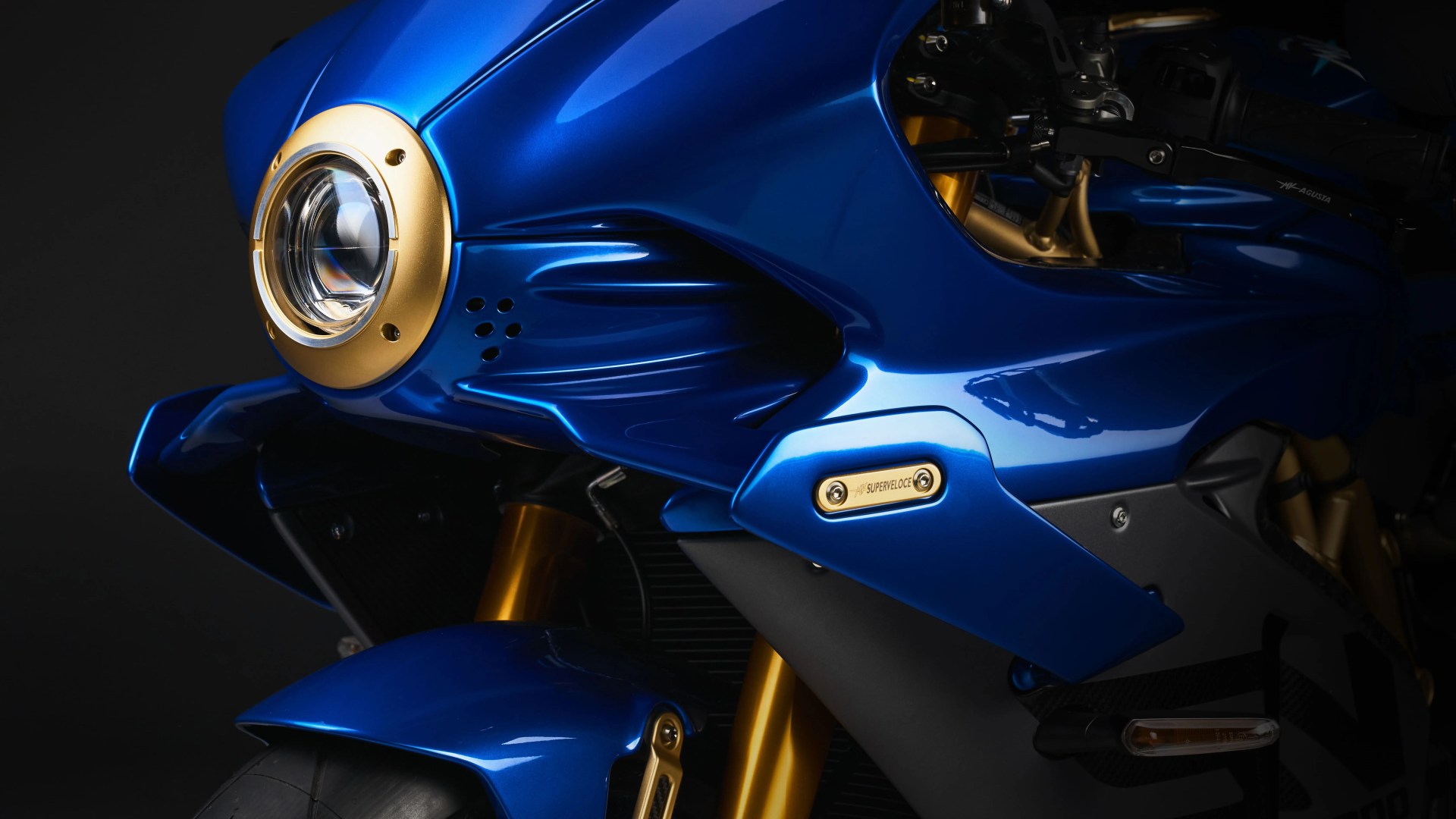 Close-up of a blue motorcycle front fairing with gold accents and a round headlight.