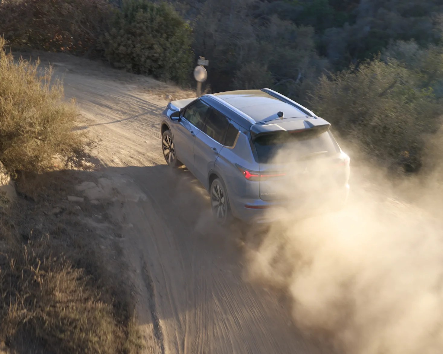 Blue SUV kicking up dust while driving on a dirt road surrounded by dry bushes.