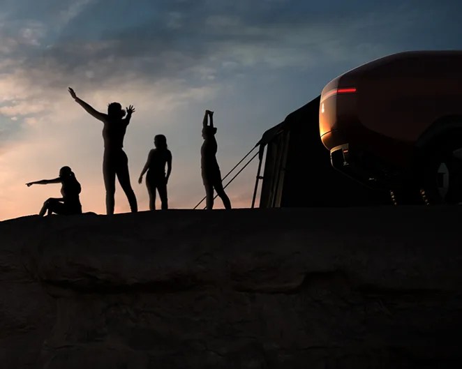 Silhouettes of four people on a rocky ledge near a vehicle and tent at sunset.