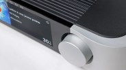 Close-up of a silver volume knob and digital display showing music track details on a black and silver audio device.