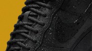 Close-up of a black sneaker with water droplets on the surface against a mustard yellow background.