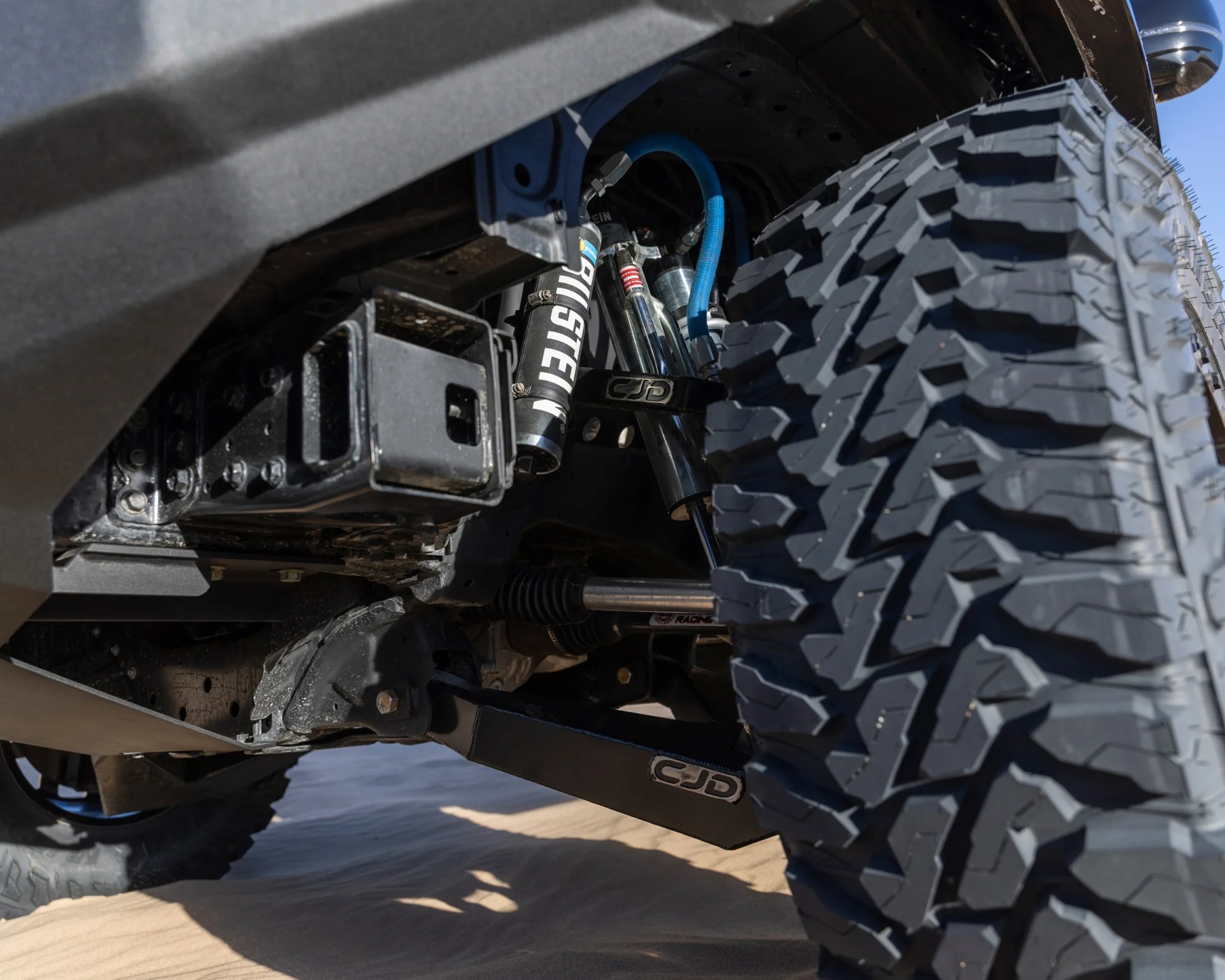Off-road vehicle suspension system with Bilstein shock absorbers and large all-terrain tire on sandy ground.