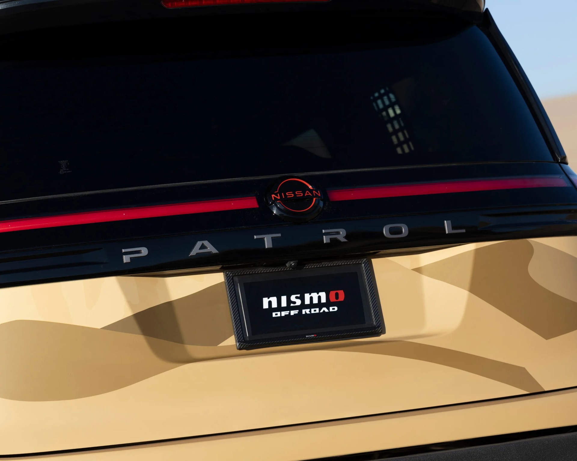 Rear view of a beige Nissan Patrol with black and red trim and a "nismo OFF ROAD" license plate frame.