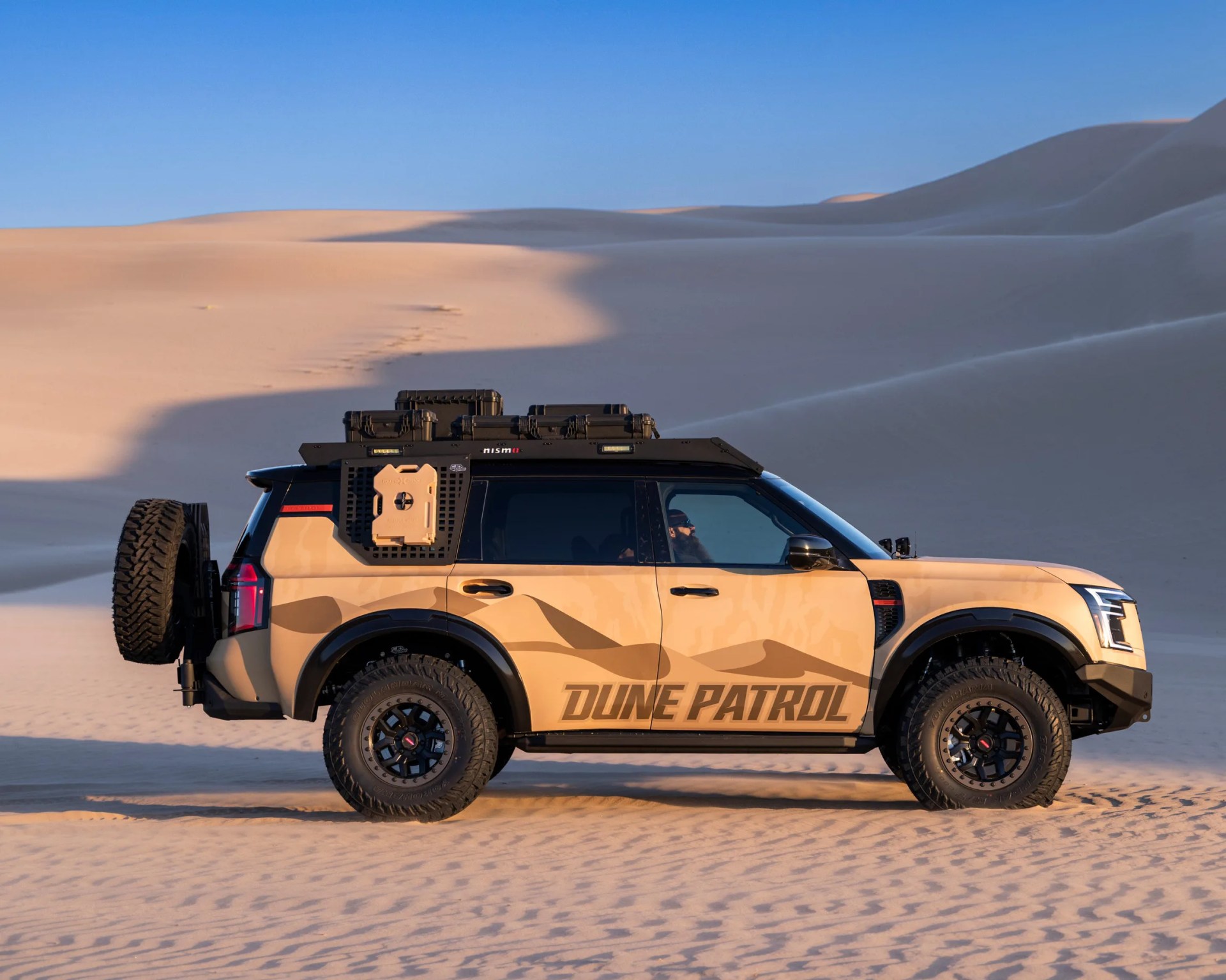 Tan and black off-road SUV with "Dune Patrol" decal and roof storage parked on sand dunes.
