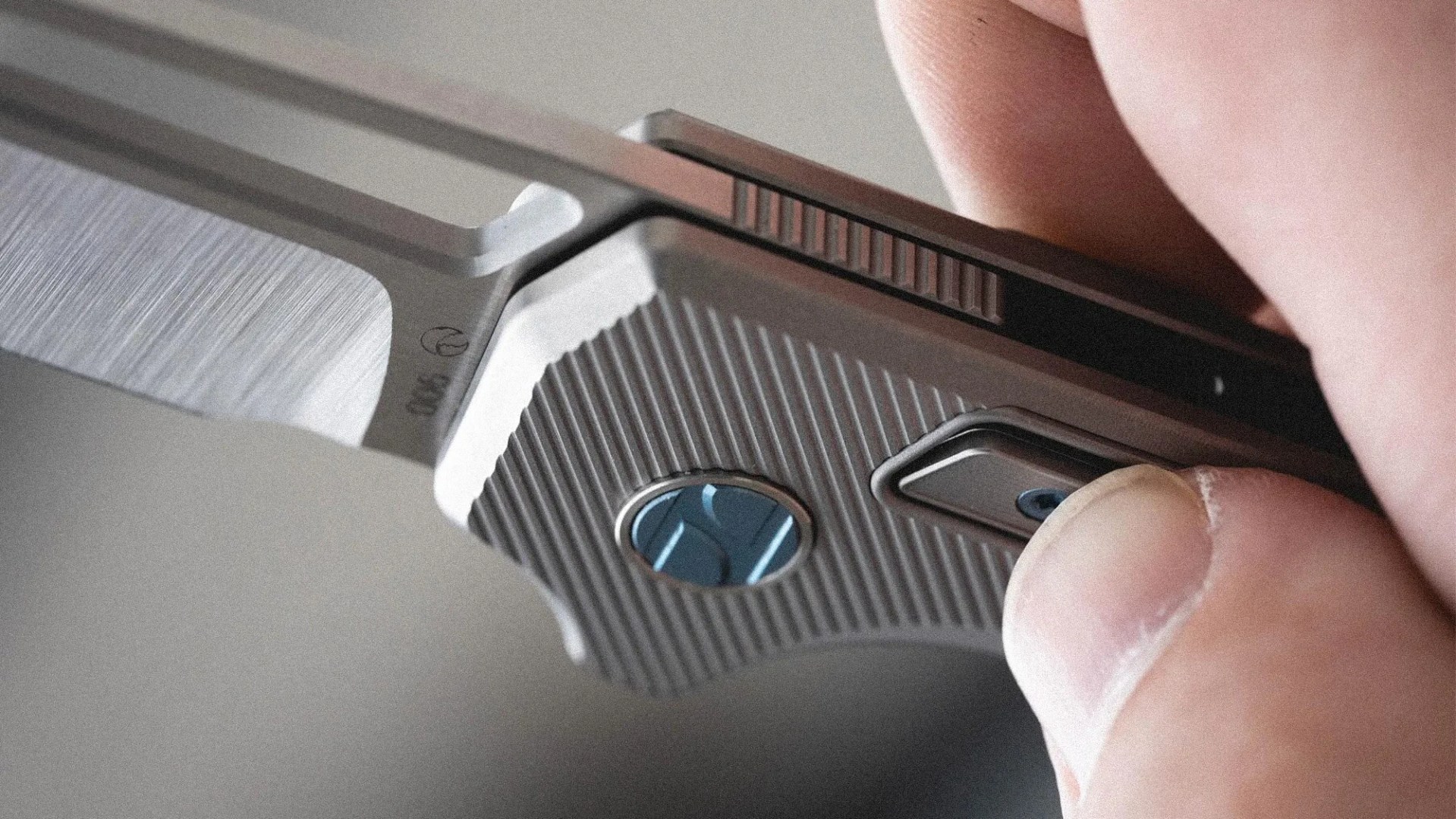 Close-up of a hand holding a silver folding knife with a textured handle and a blue circular emblem.