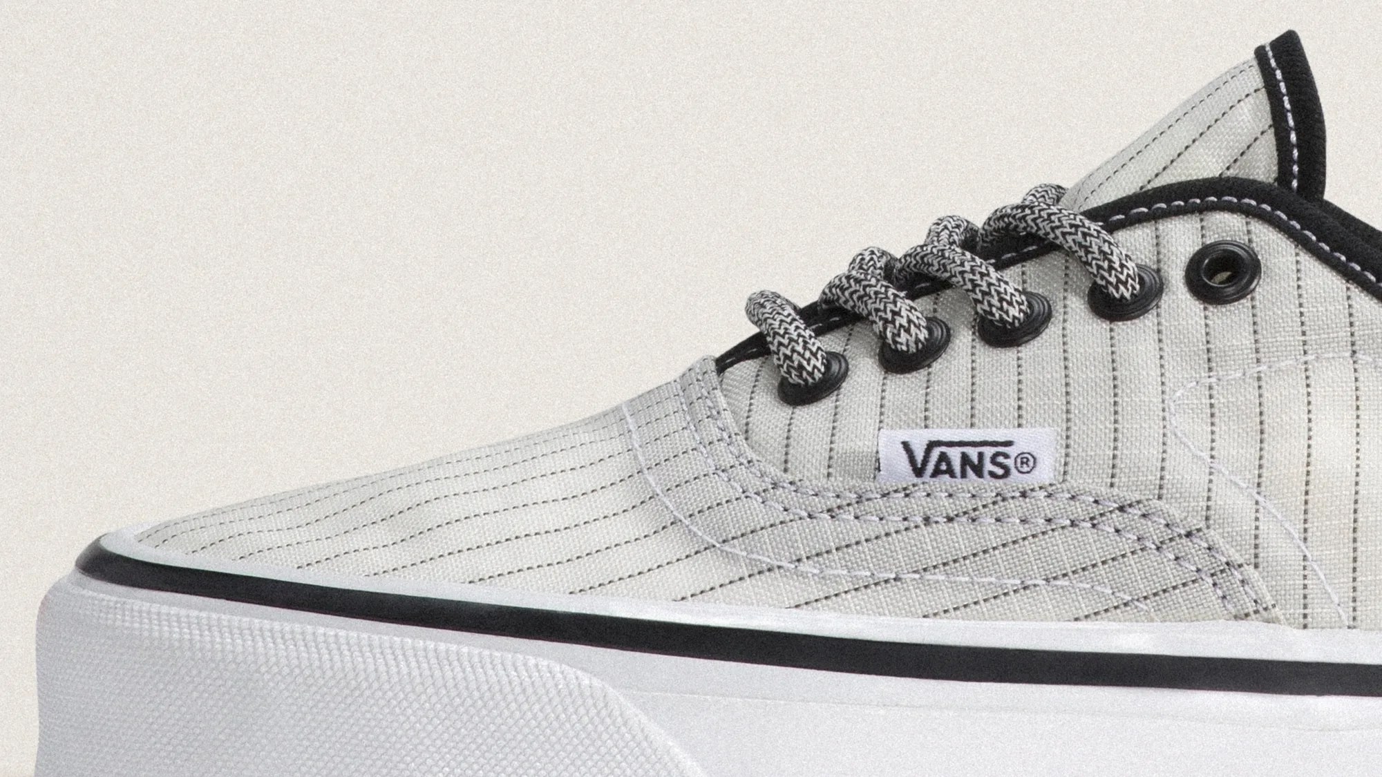Close-up of a white Vans sneaker with black pinstripes, black and white laces, and a thick white sole with a black stripe.