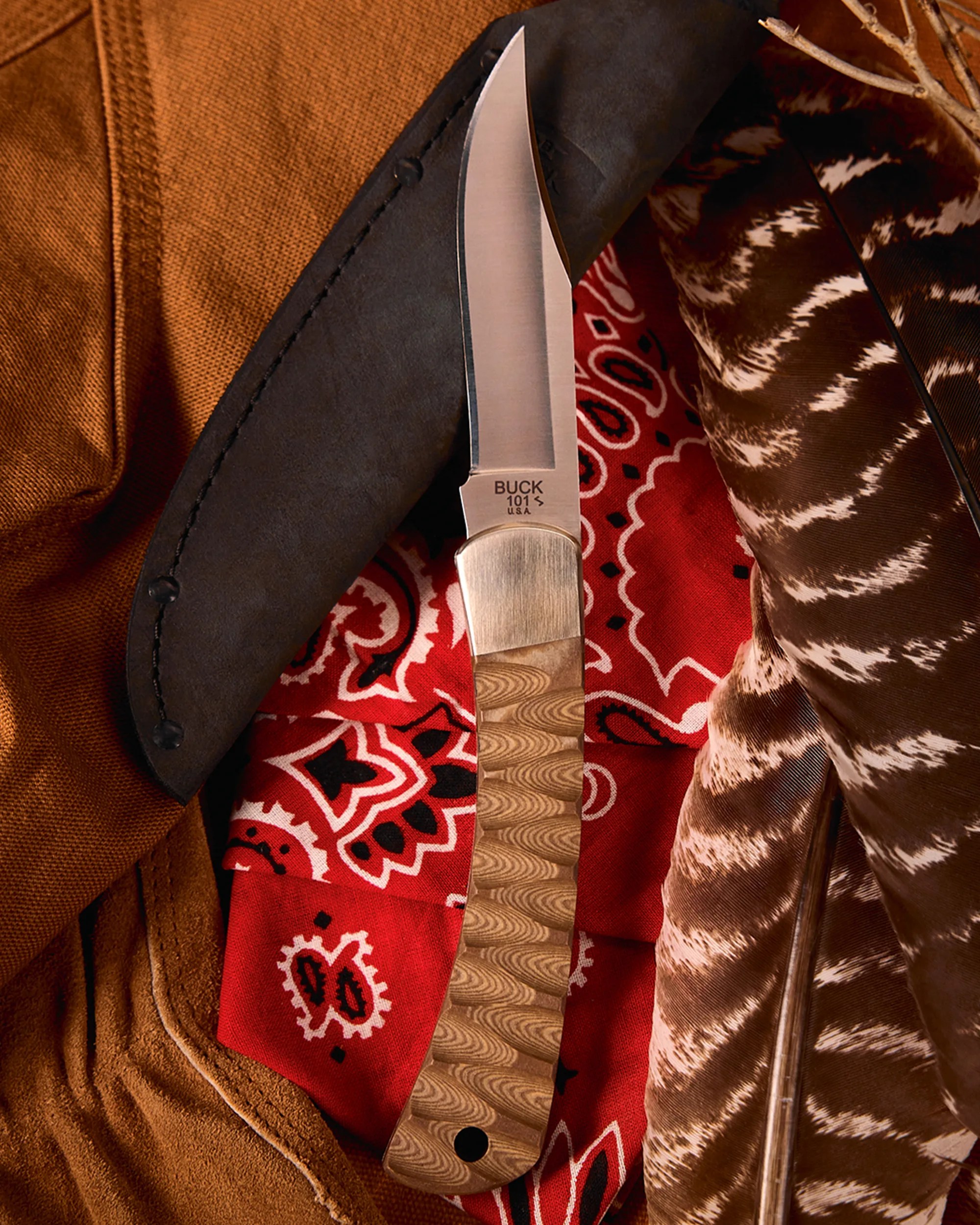 Buck 101 S fixed blade knife with wood grain handle resting on a red bandana and brown leather sheath.