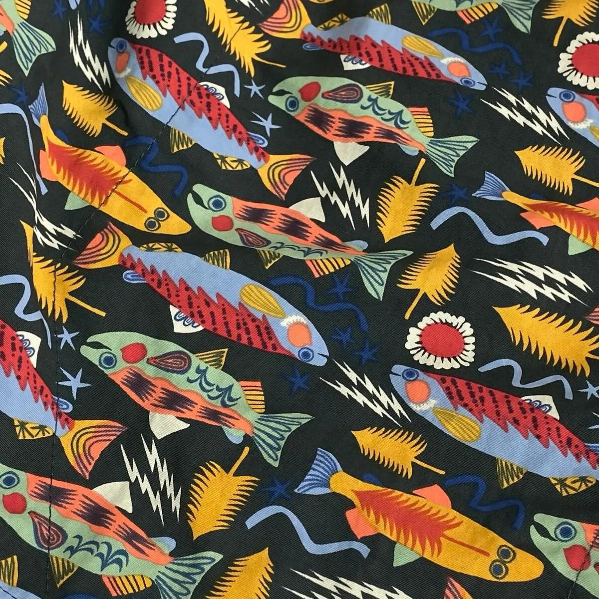 Fabric with a colorful fish and abstract leaf pattern on a black background.