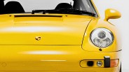 Front view of a yellow Porsche sports car showing the hood, windshield, right headlight, and side mirror.
