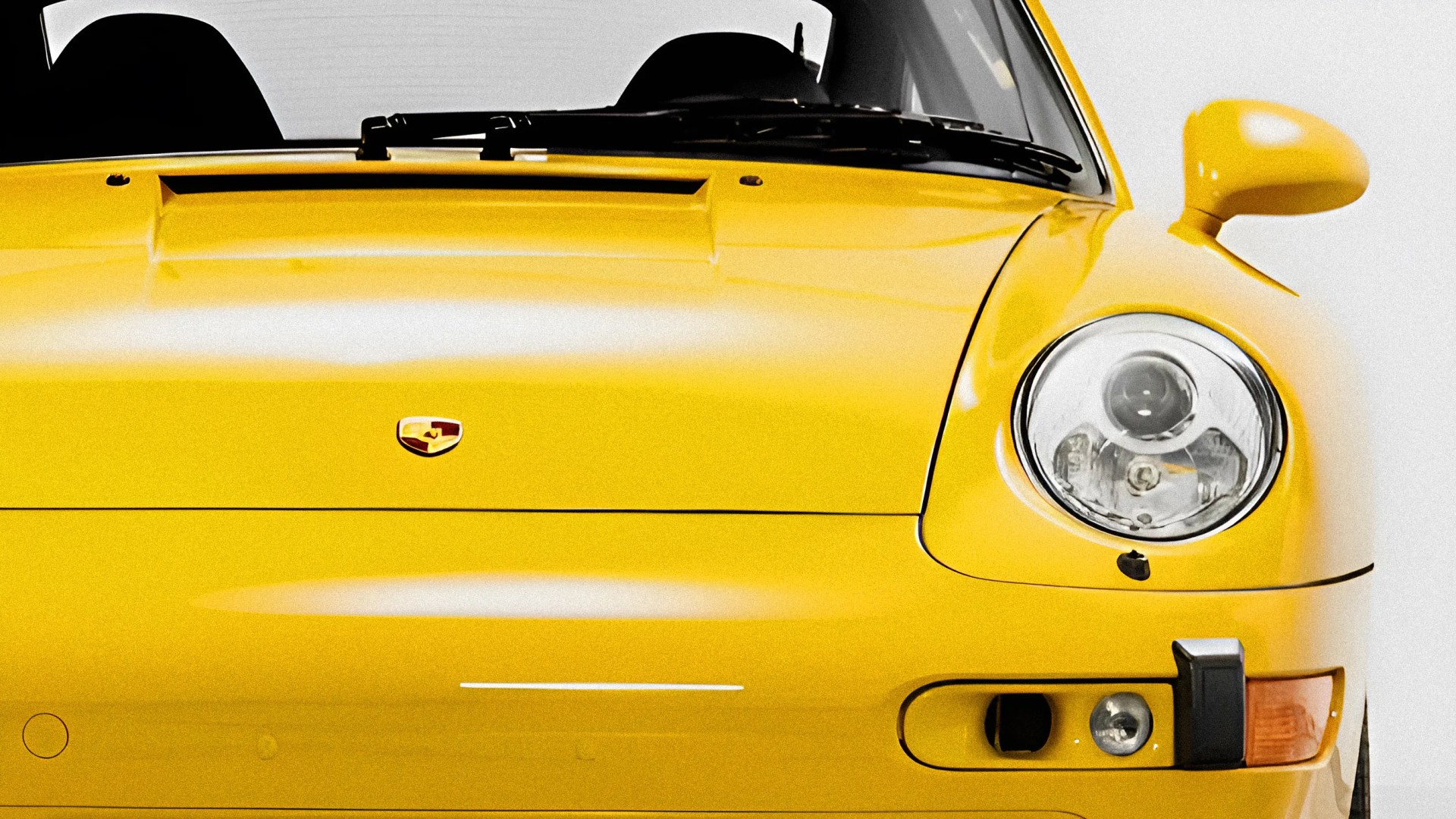 Front view of a yellow Porsche sports car showing the hood, windshield, right headlight, and side mirror.