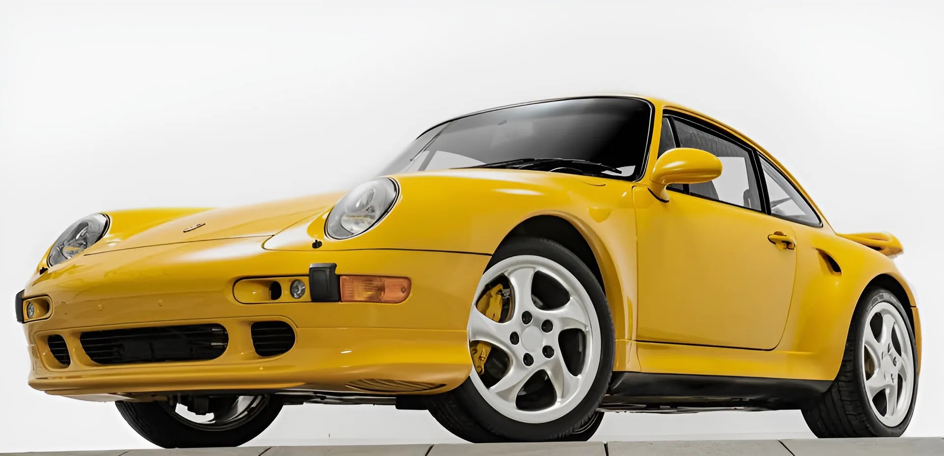 Yellow Porsche 911 sports car with white five-spoke wheels and black tinted windows on a white background.