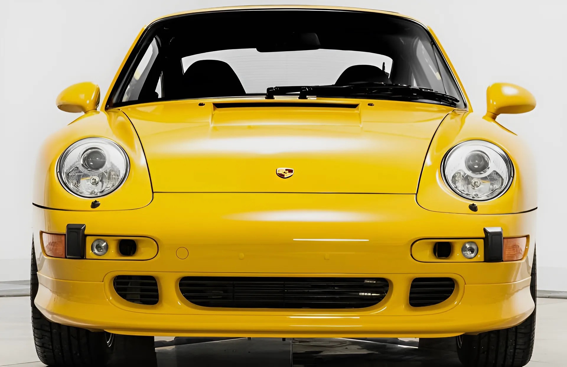 Front view of a yellow Porsche 911 sports car with round headlights and black grille vents.