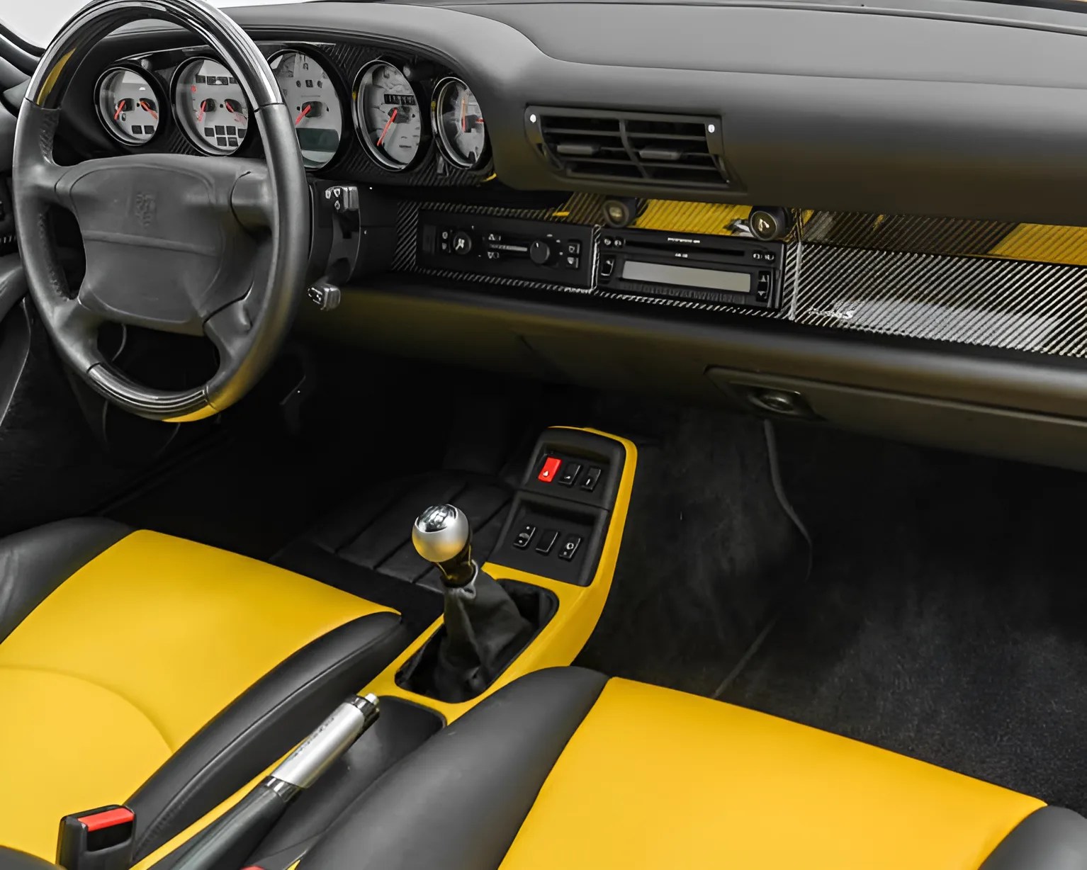Black and yellow leather car seats with a manual gear shift and carbon fiber dashboard trim.