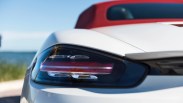 Close-up of a white sports car's rear left taillight with a red convertible roof in the background.