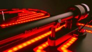 Close-up of a black Pro-Ject turntable tonearm illuminated by red LED lights on a dark background.