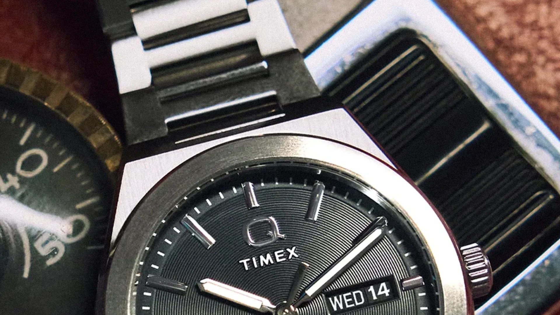 Close-up of a Timex wristwatch with a black textured dial, silver hour markers, and a date display showing "WED 14".
