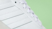 Close-up of a white sneaker with zigzag-stitched stripes and white laces on a light green background.