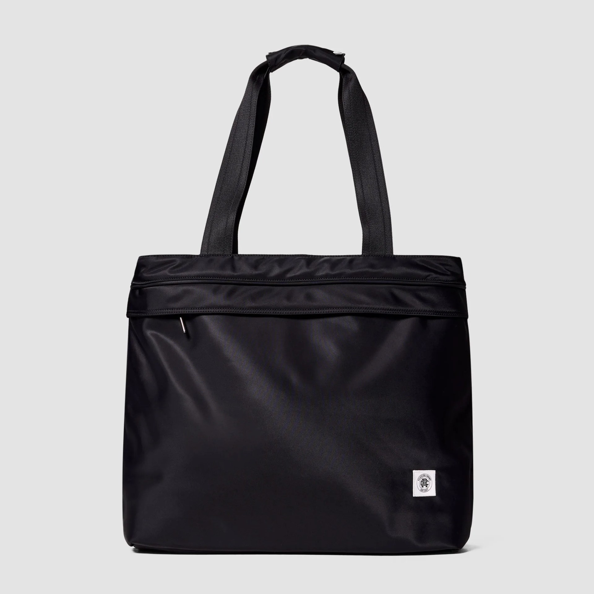Black tote bag with wide handles, a top zipper pocket, and a small white logo patch on the front bottom right.