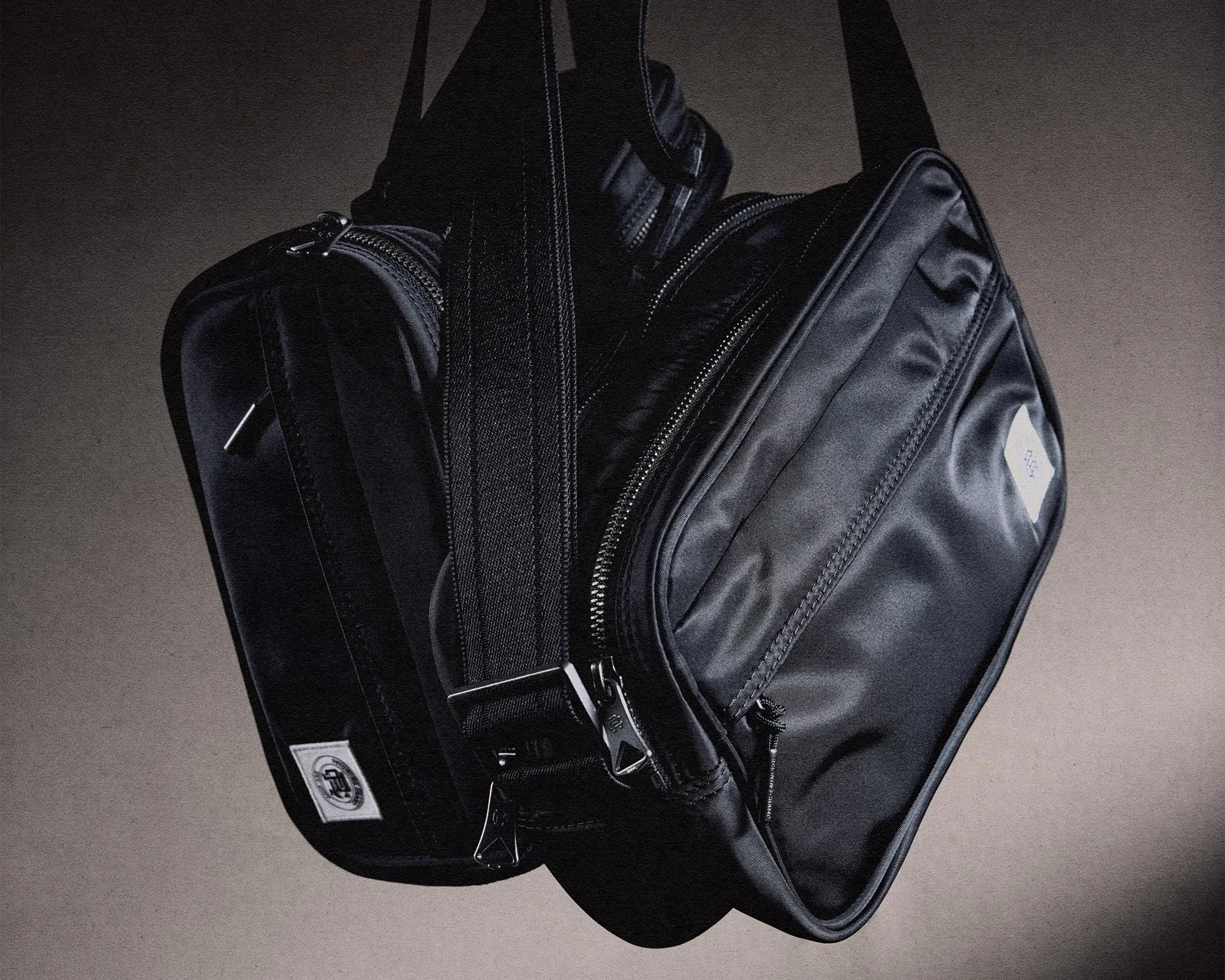 Two black nylon crossbody bags with silver zippers hanging against a neutral background.