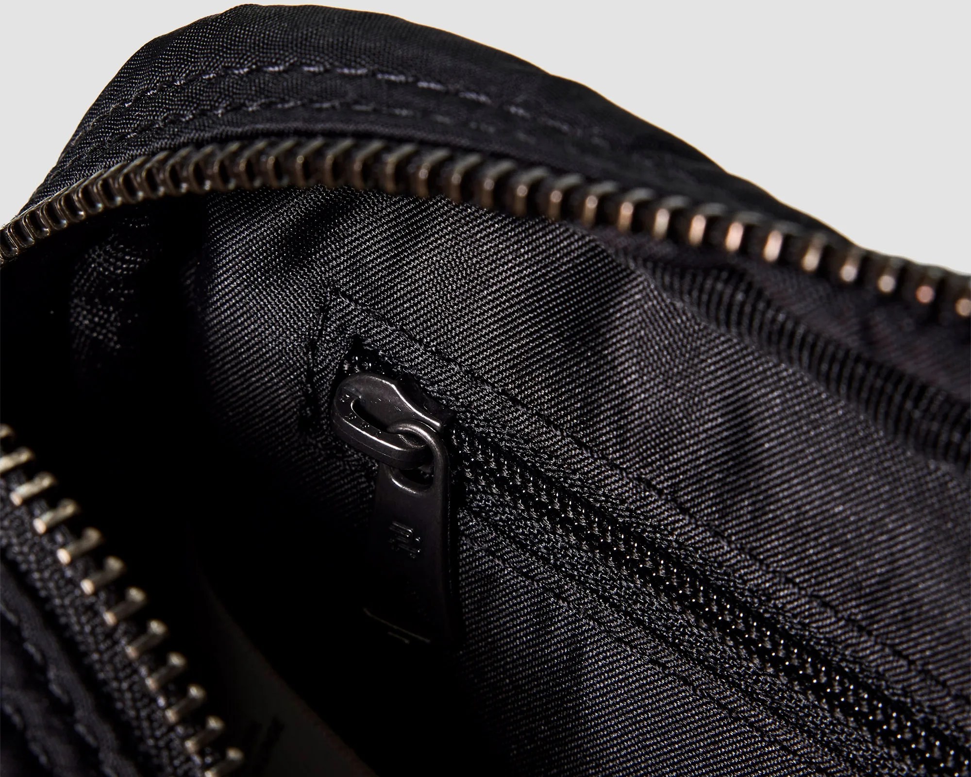 Close-up of a black fabric bag interior showing a small zippered pocket with a black zipper pull.