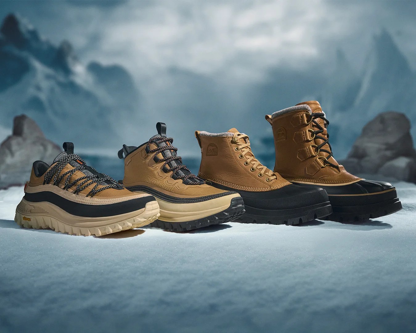 Four pairs of tan and black winter boots and shoes with thick soles on snow with a mountainous background.