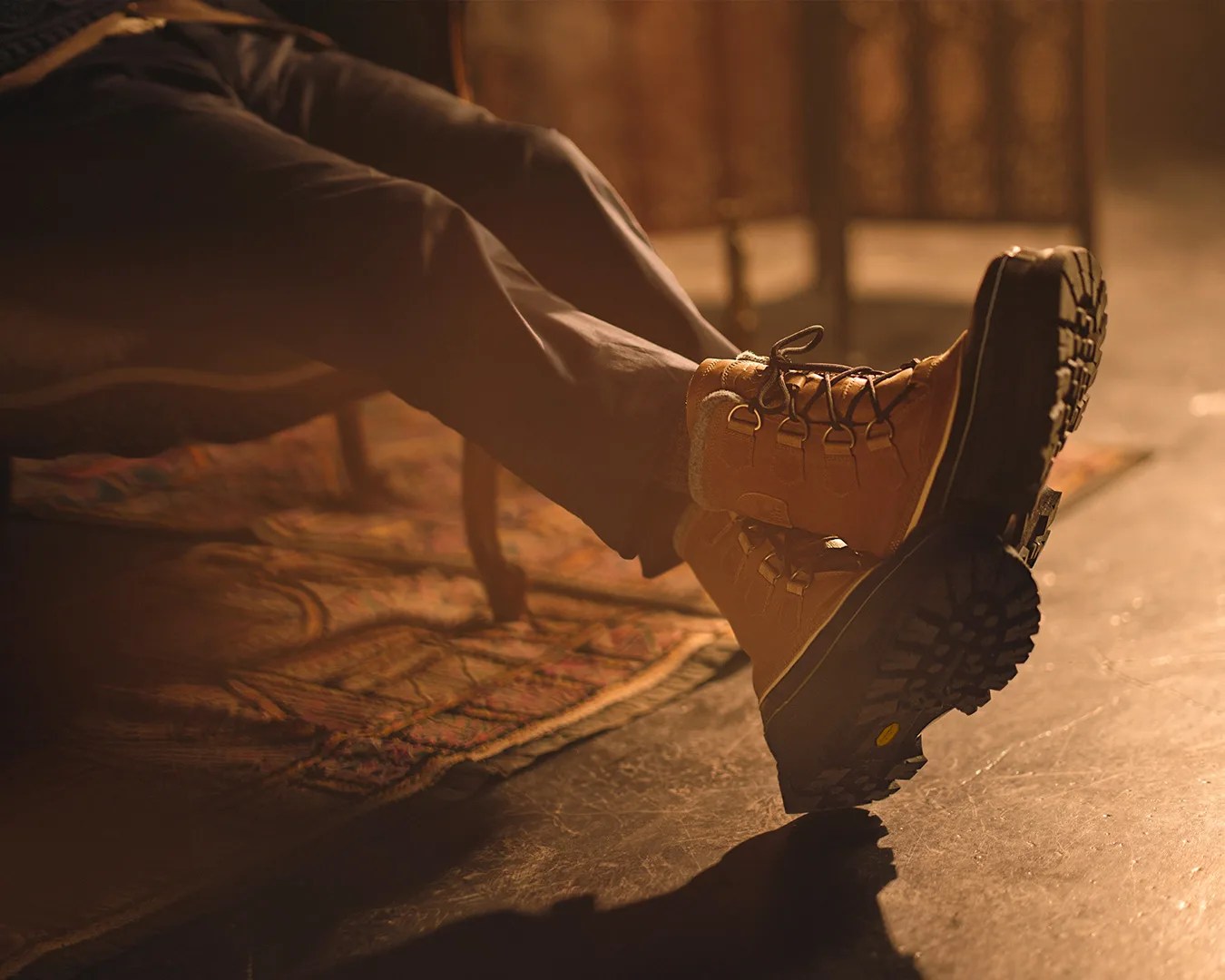 Brown leather winter boots with black rugged soles worn by a person sitting indoors on a patterned rug.