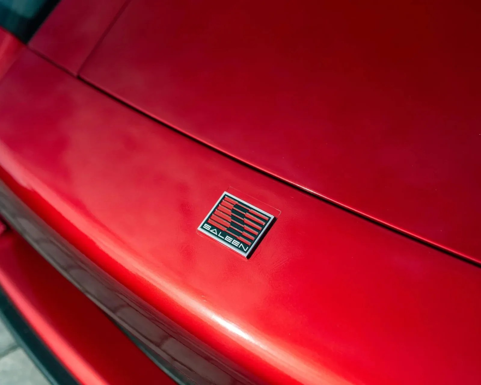 Close-up of a red car hood with a Saleen logo badge featuring red and black stripes.