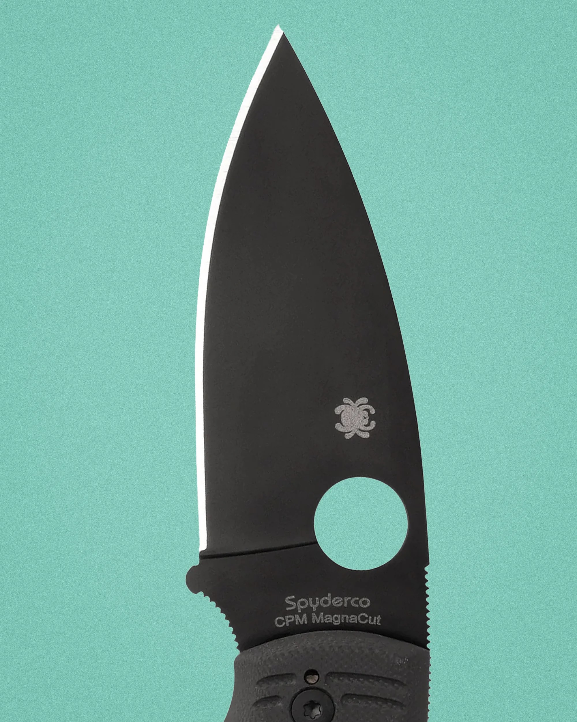 Black Spyderco CPM MagnaCut knife blade with a round hole near the handle on a teal background.