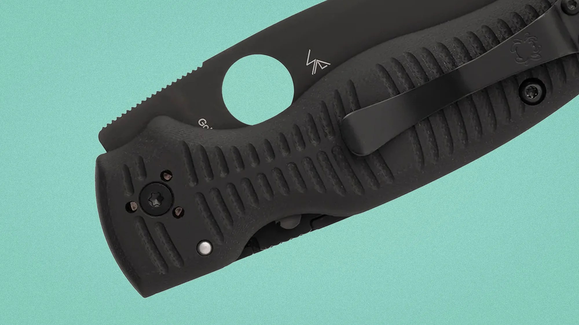 Black folding knife with textured grip and metal clip on a teal background.