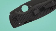 Black folding knife with textured grip and metal clip on a teal background.
