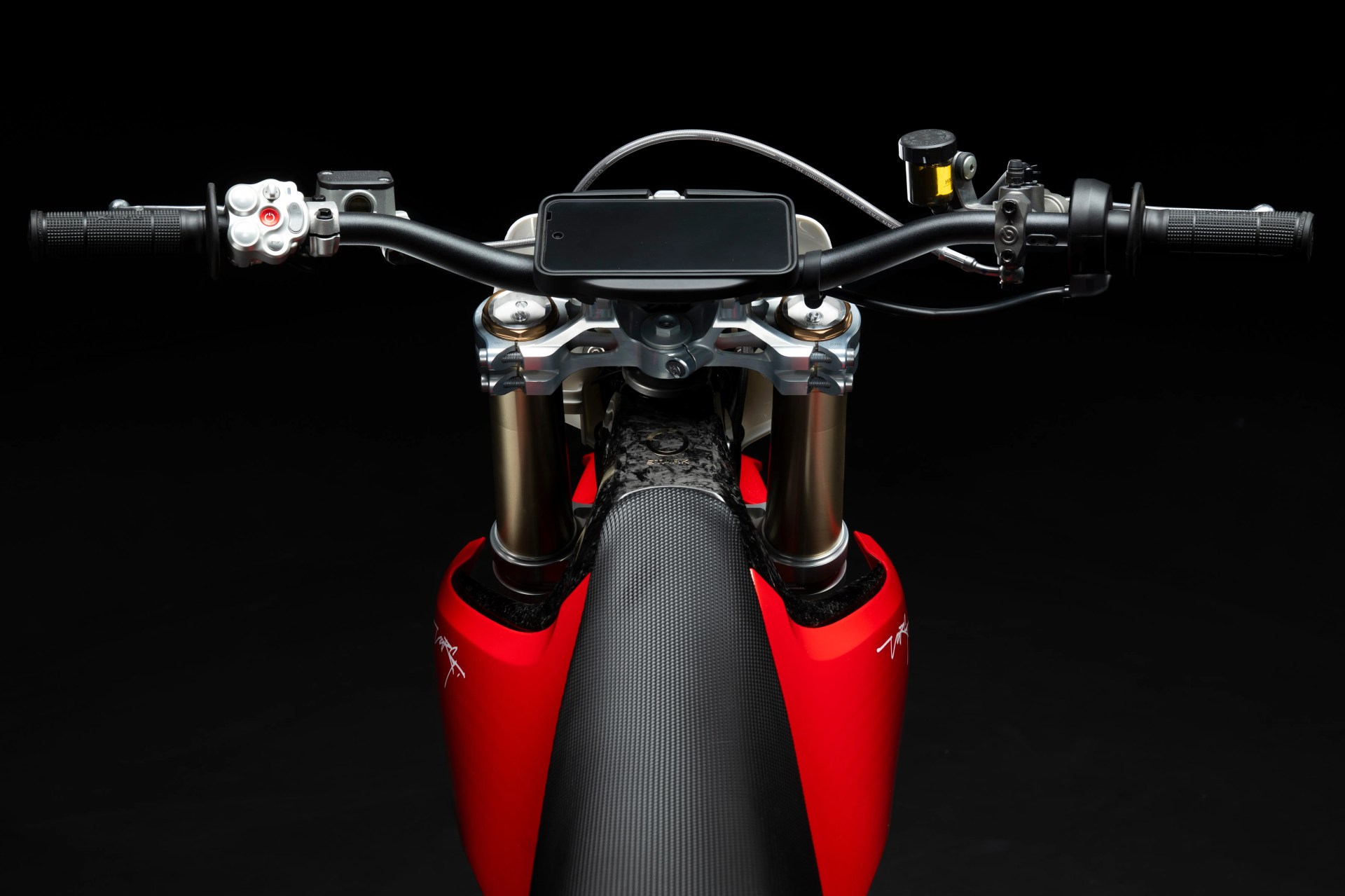 Black smartphone mounted on black handlebars of a red and black motorcycle against a black background.