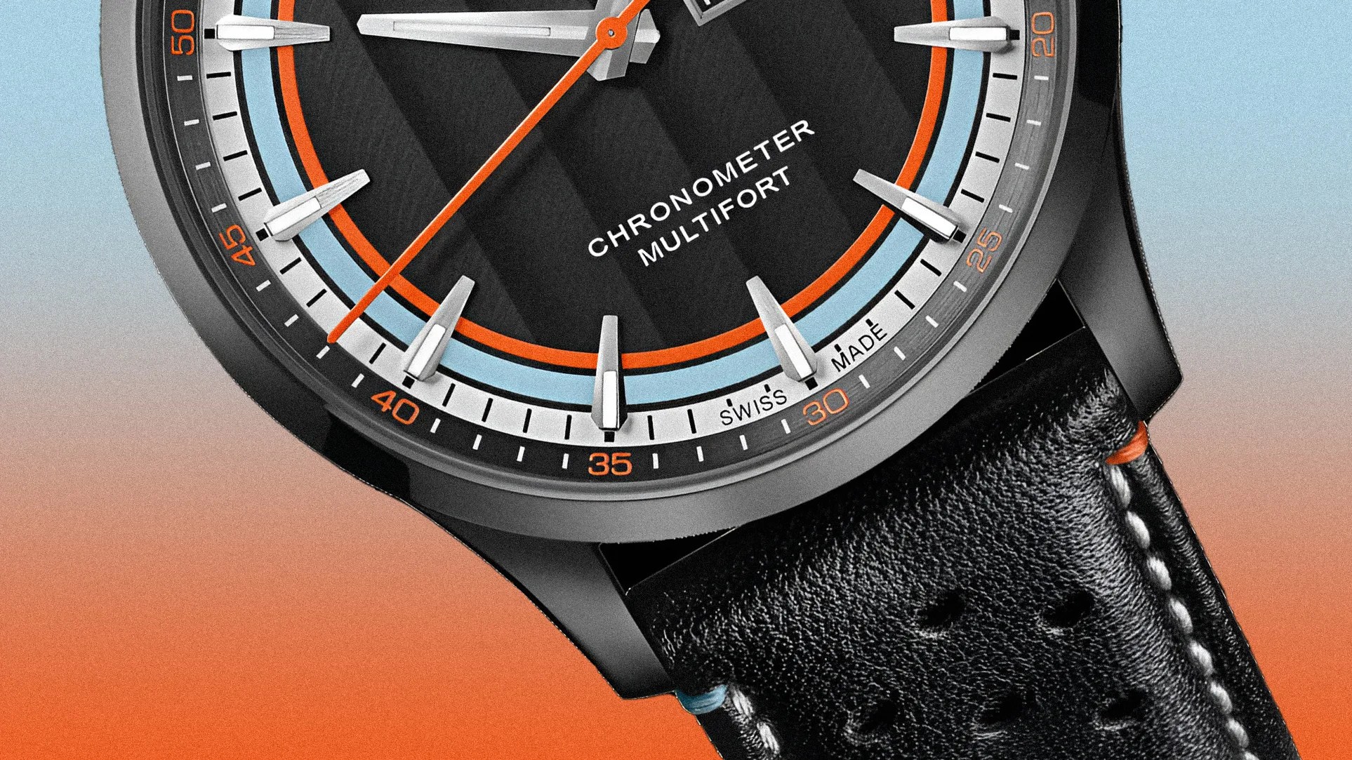 Close-up of a black watch face with orange and light blue accents, silver hour markers, and black leather strap with white stitching.