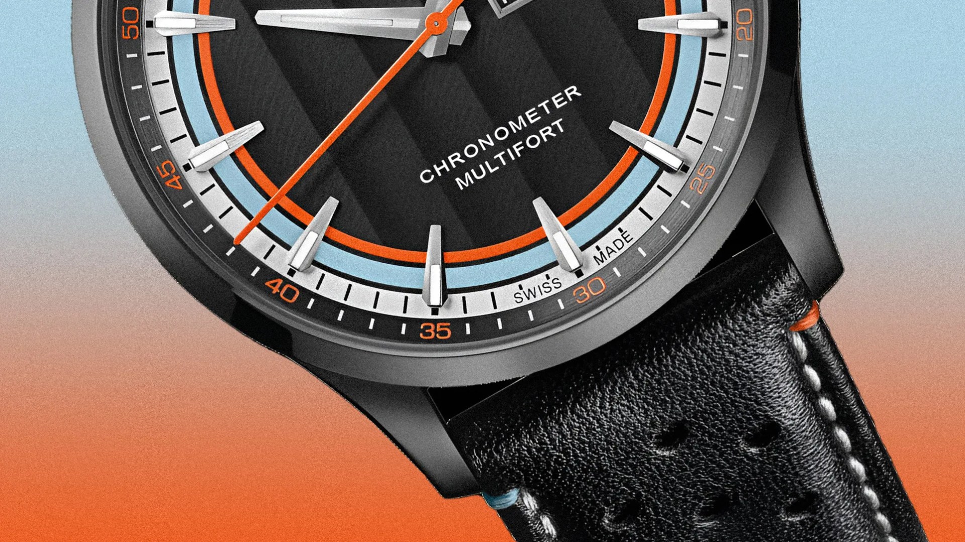 Close-up of a black watch face with orange and light blue accents, silver hour markers, and black leather strap with white stitching.