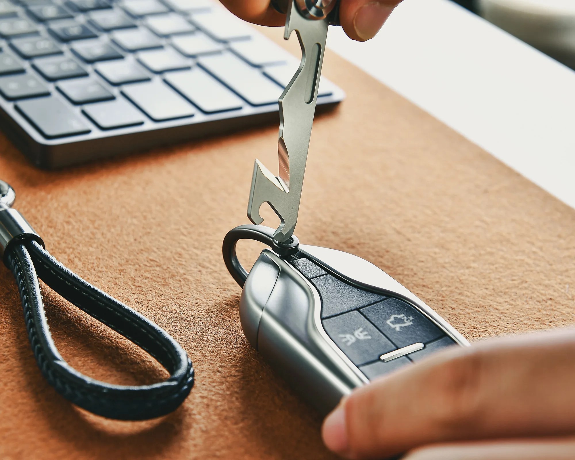 Silver multi-tool being used to press a button on a black and silver car key fob on a brown surface near a keyboard.