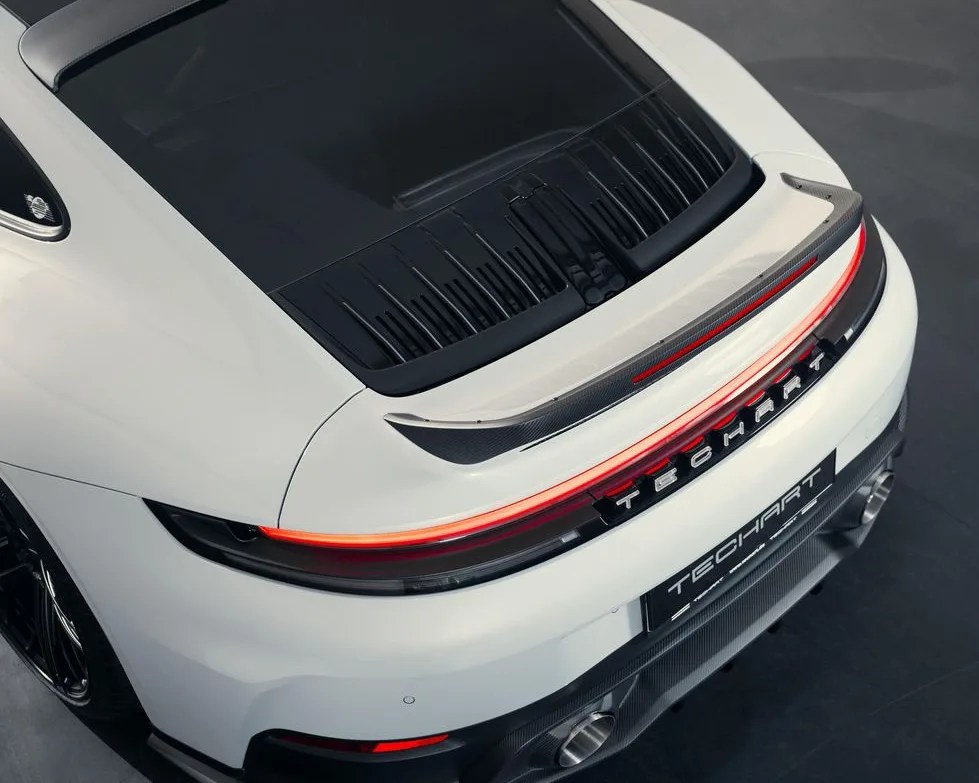 Rear view of a white TechArt sports car with illuminated taillights and carbon fiber spoiler and diffuser.