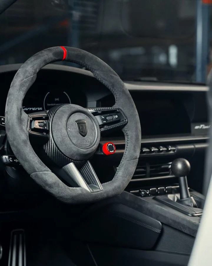 Black suede steering wheel with red center marker and carbon fiber accents inside a car.