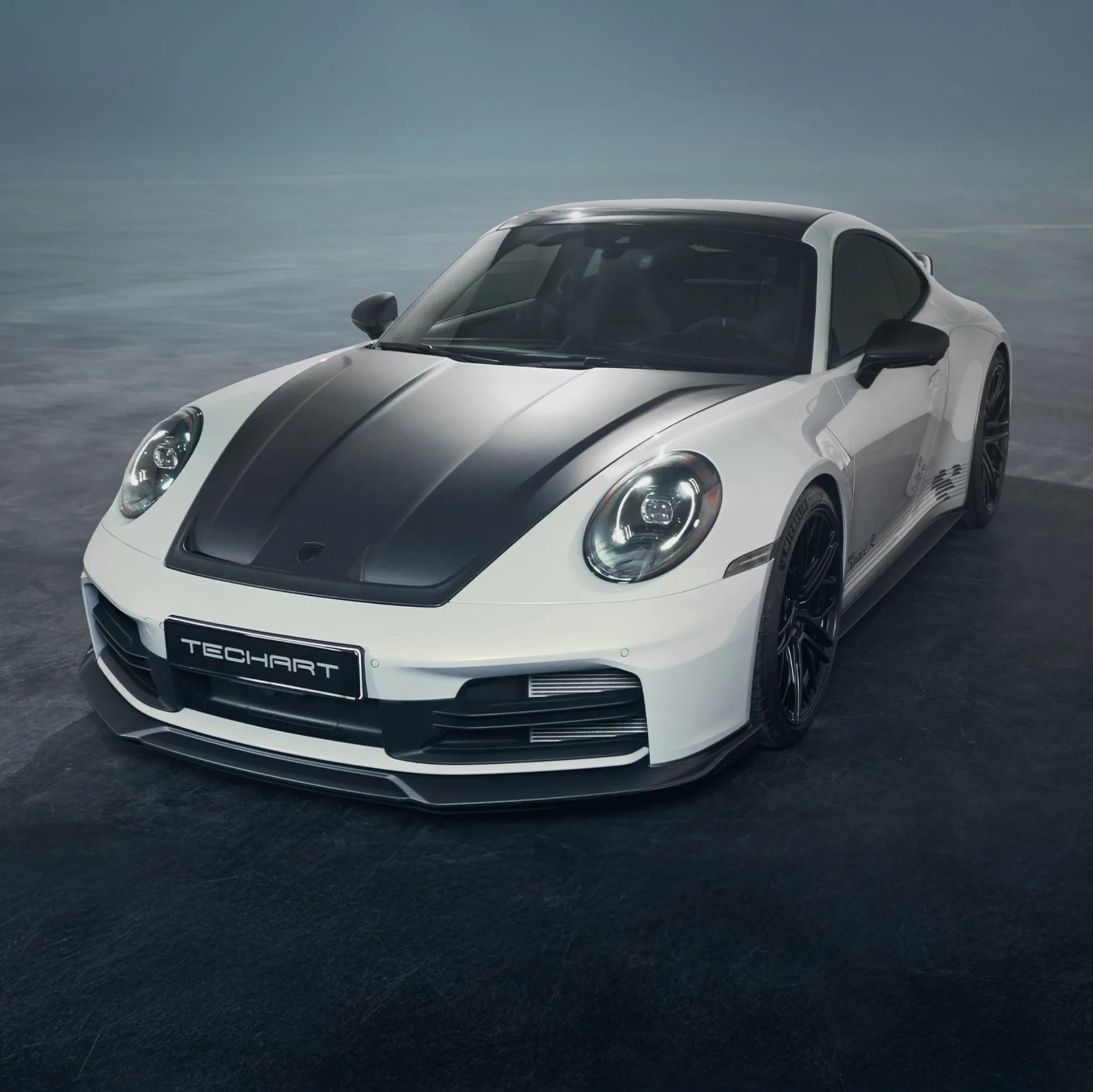 White and black TechArt sports car with carbon fiber hood and black wheels on a dark floor.