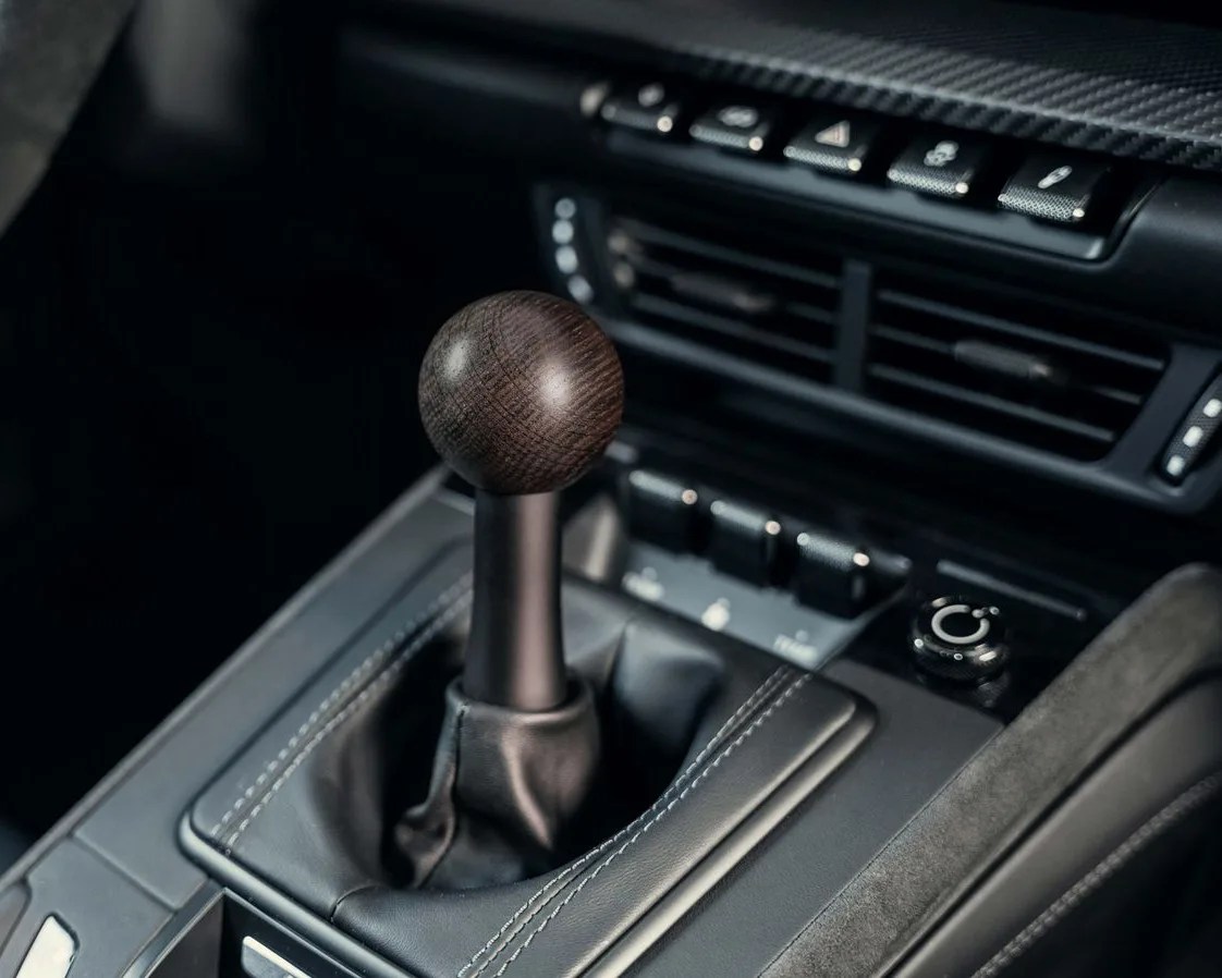 Car interior showing a manual gear shift with a dark wood spherical knob and black leather boot.