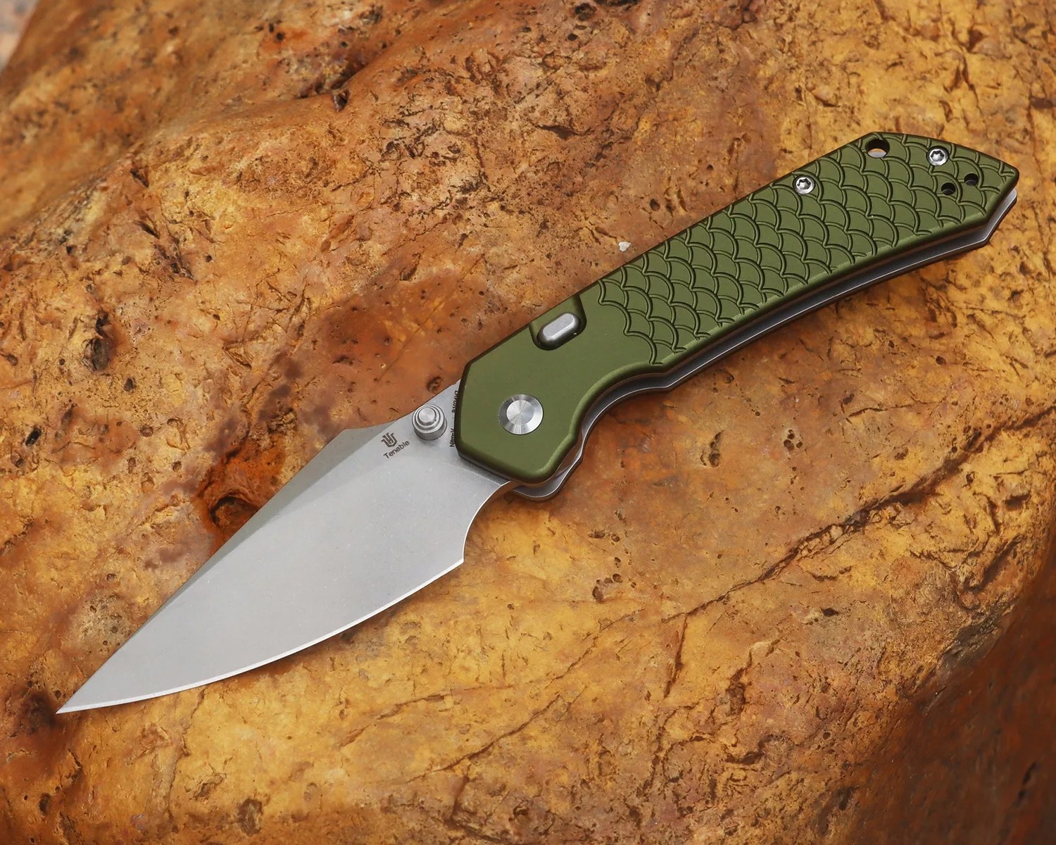 Folding knife with a silver blade and olive green textured handle resting on a brown rock.