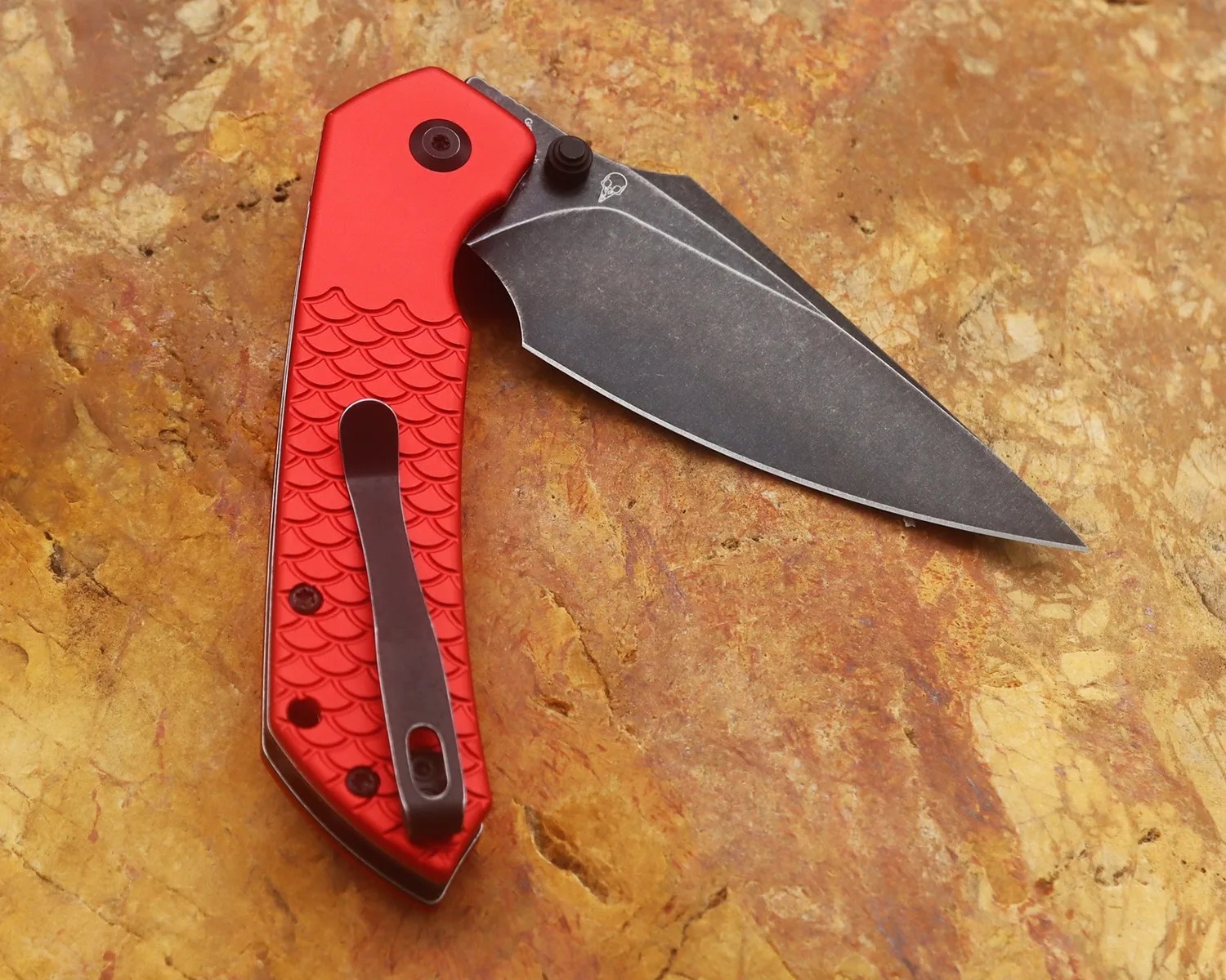 Folding knife with a black stonewashed blade and a red textured handle featuring a black pocket clip.