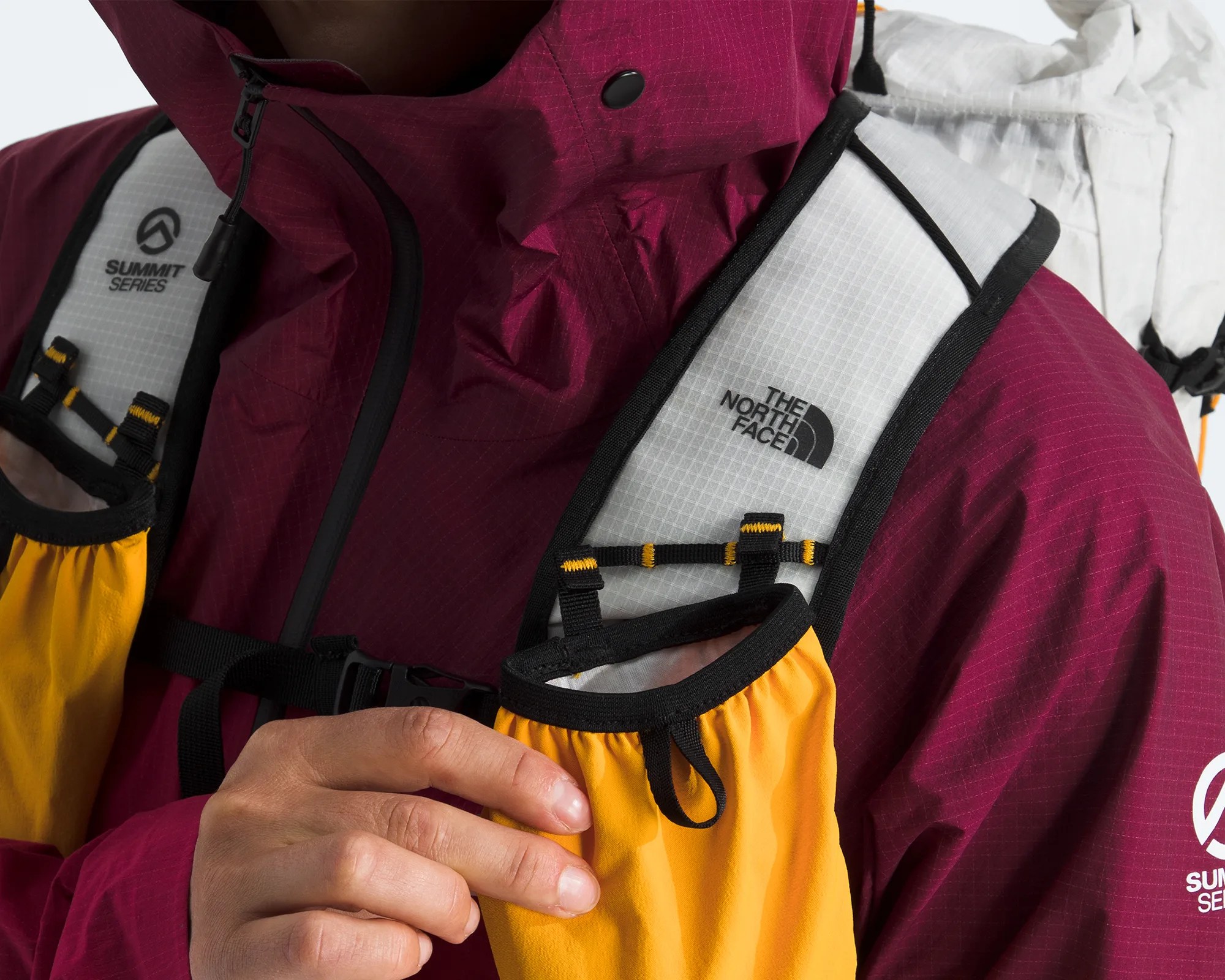 Close-up of a person wearing a maroon Summit Series jacket and adjusting a yellow and white The North Face backpack strap.