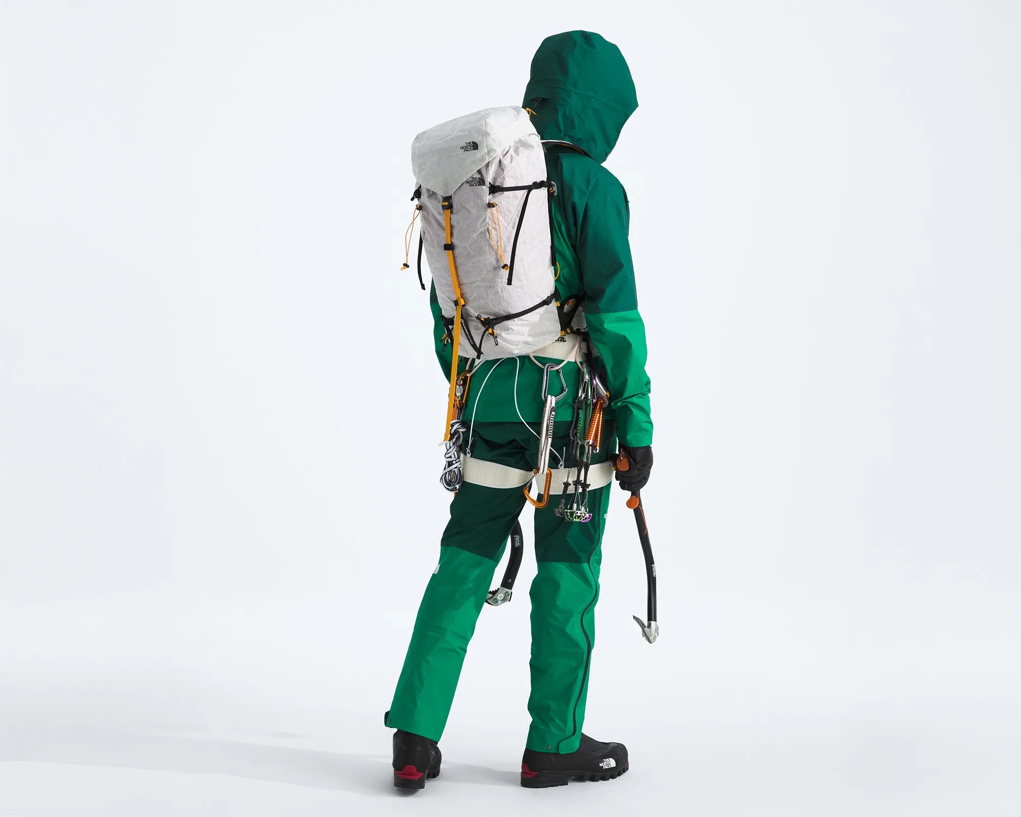 Person wearing green mountaineering gear with a white North Face backpack and climbing equipment attached to a harness.